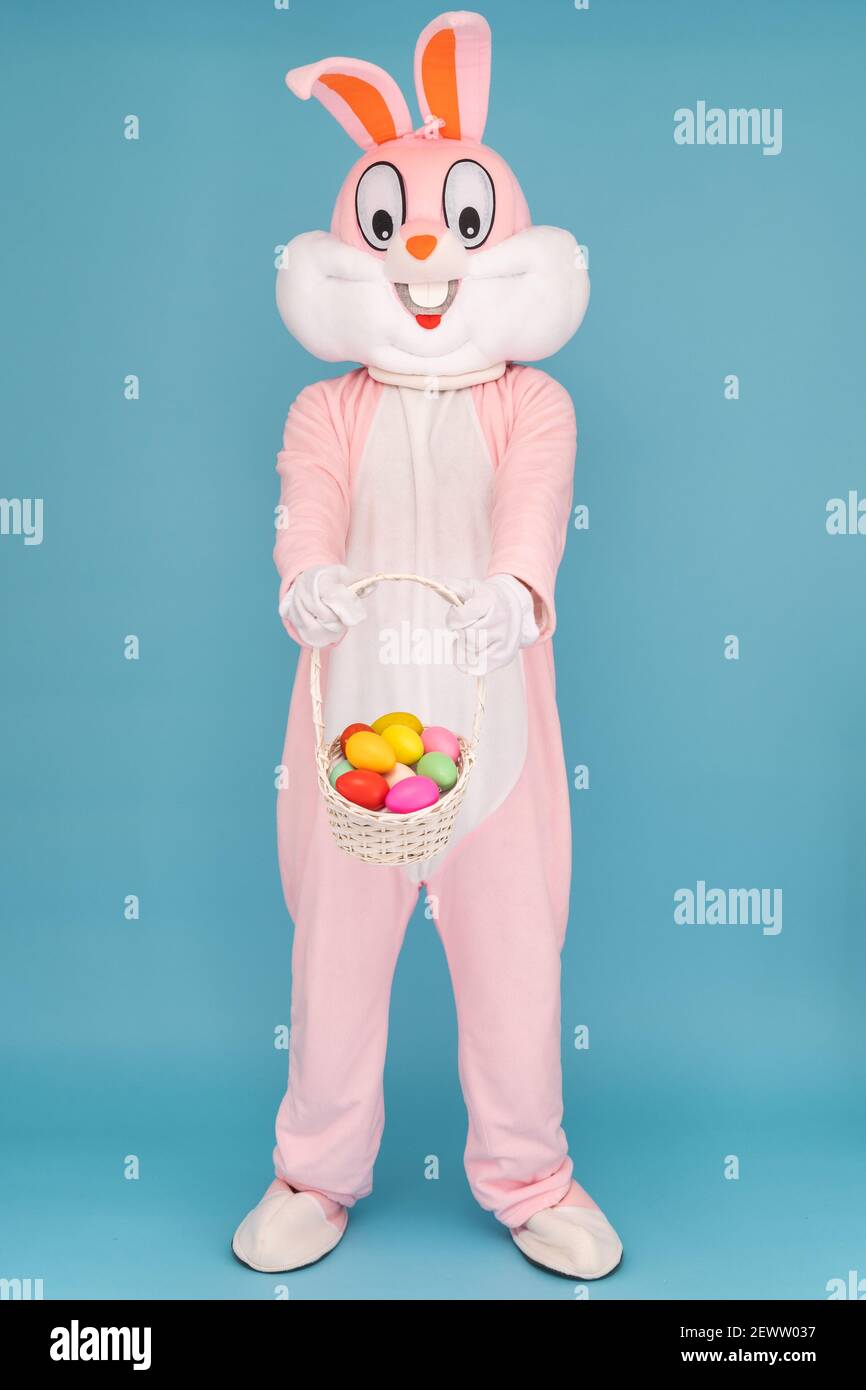 Osterhase oder Kaninchen oder Hase mit Korb von bunten Eiern, Spaß haben, tanzen, feiert Frohe Ostern. Osterkaninchen isoliert auf blauem Hintergrund. Stockfoto