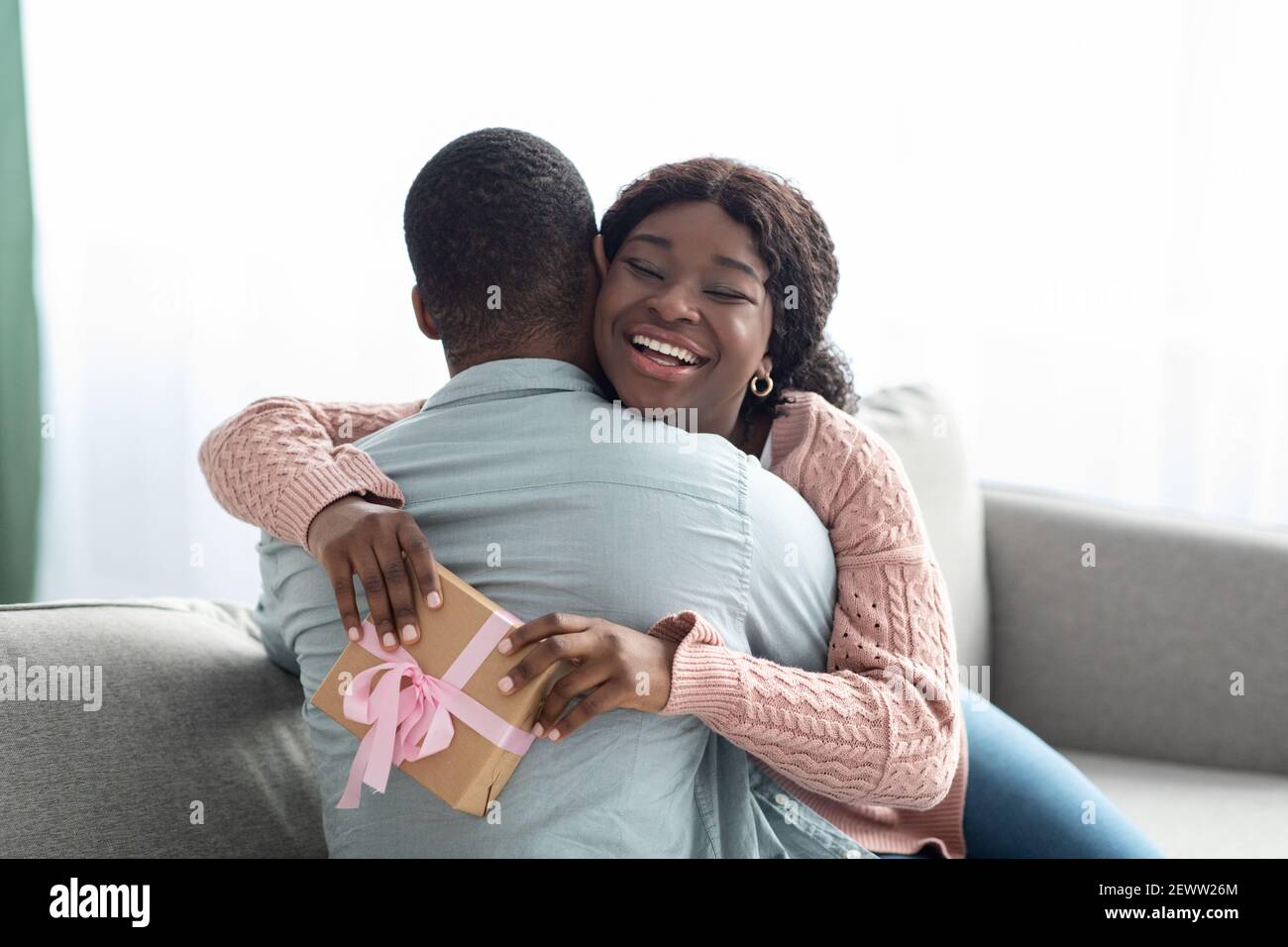 Glückliche afroamerikanische Dame mit Geschenk umarmt ihren Liebhaber Stockfoto Glückliche afroamerikanische Dame mit Geschenk umarmt ihren Liebhaber Stockfoto