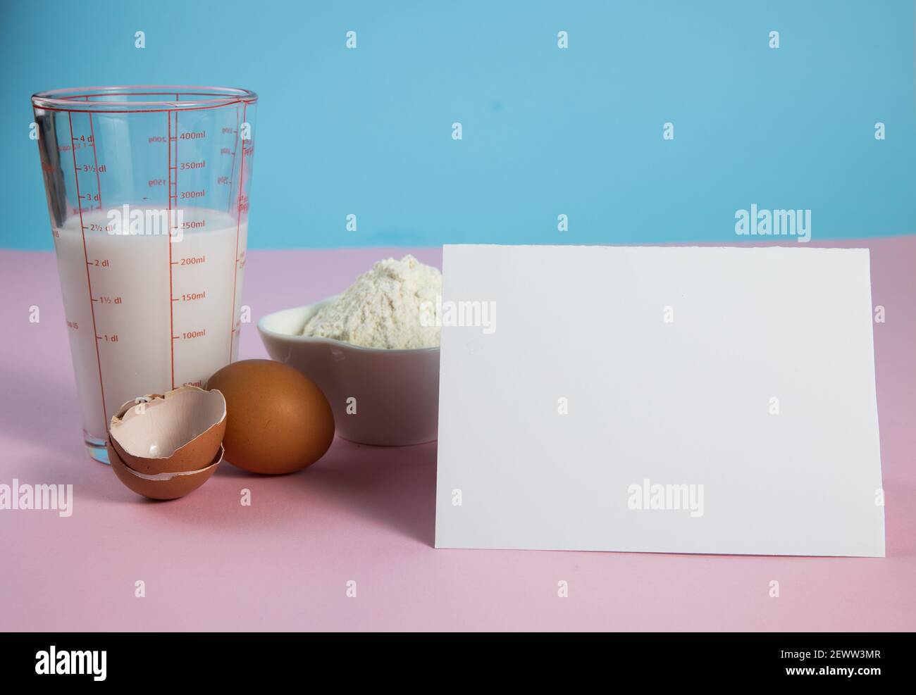Zutaten zum Backen - Eier, Mehl, Milch auf hellblauem und rosa Hintergrund Stockfoto