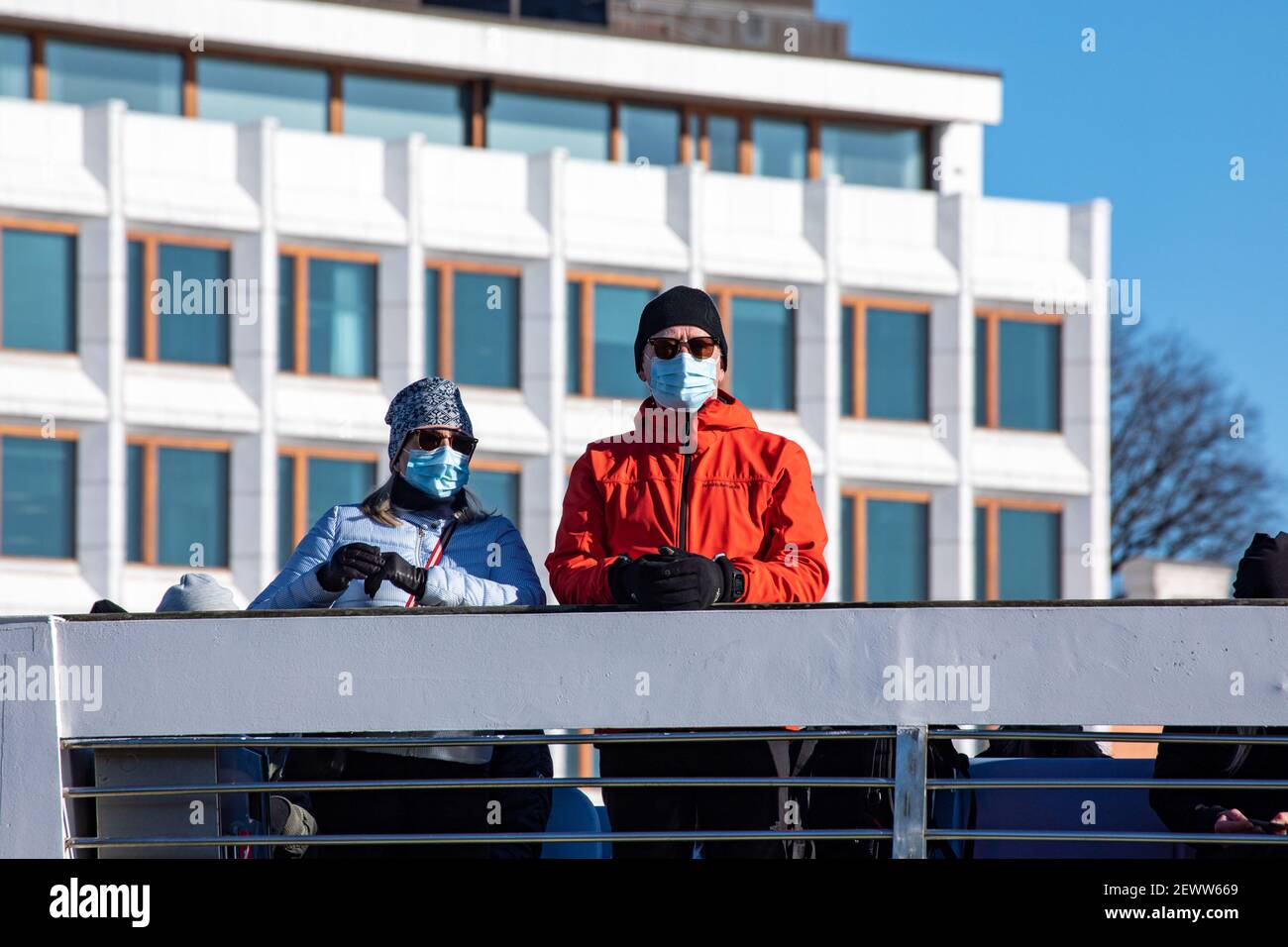 Gesichtsmaske trägt Paar auf Suomenlinna Fähre Deck mit ehemaligen Enso-Gutzeit Hauptsitz im Hintergrund in Helsinki, Finnland Stockfoto