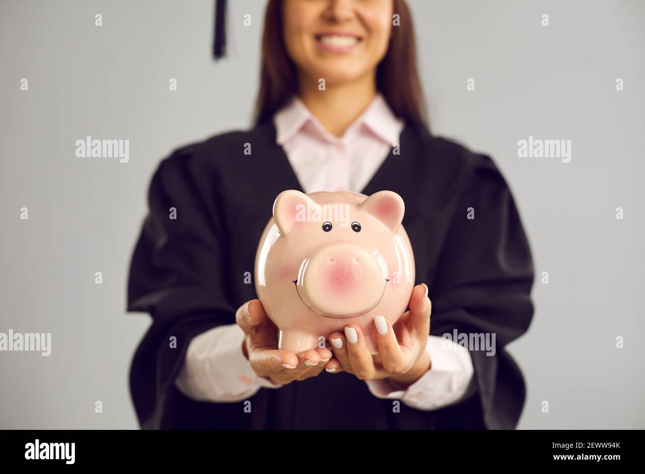 Nahaufnahme eines Sparschweines in den Händen einer Schülerin auf grauem Hintergrund. Bildungsfonds. Stockfoto