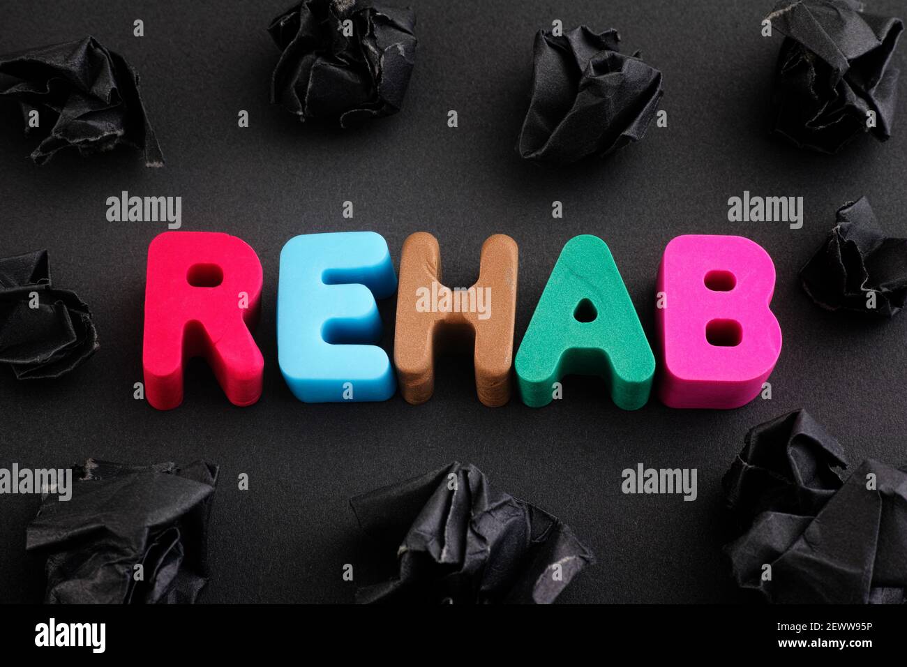 Das Wort Rehab aus Fimo Buchstaben mit einigen schwarzen zerknitterten Papierkugeln um ihn herum. Nahaufnahme. Stockfoto