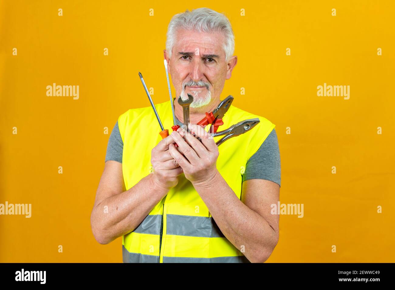 Porträt eines reifen Arbeiters mit Reflektorweste mit Werkzeugen Isoliert auf gelbem Hintergrund Stockfoto