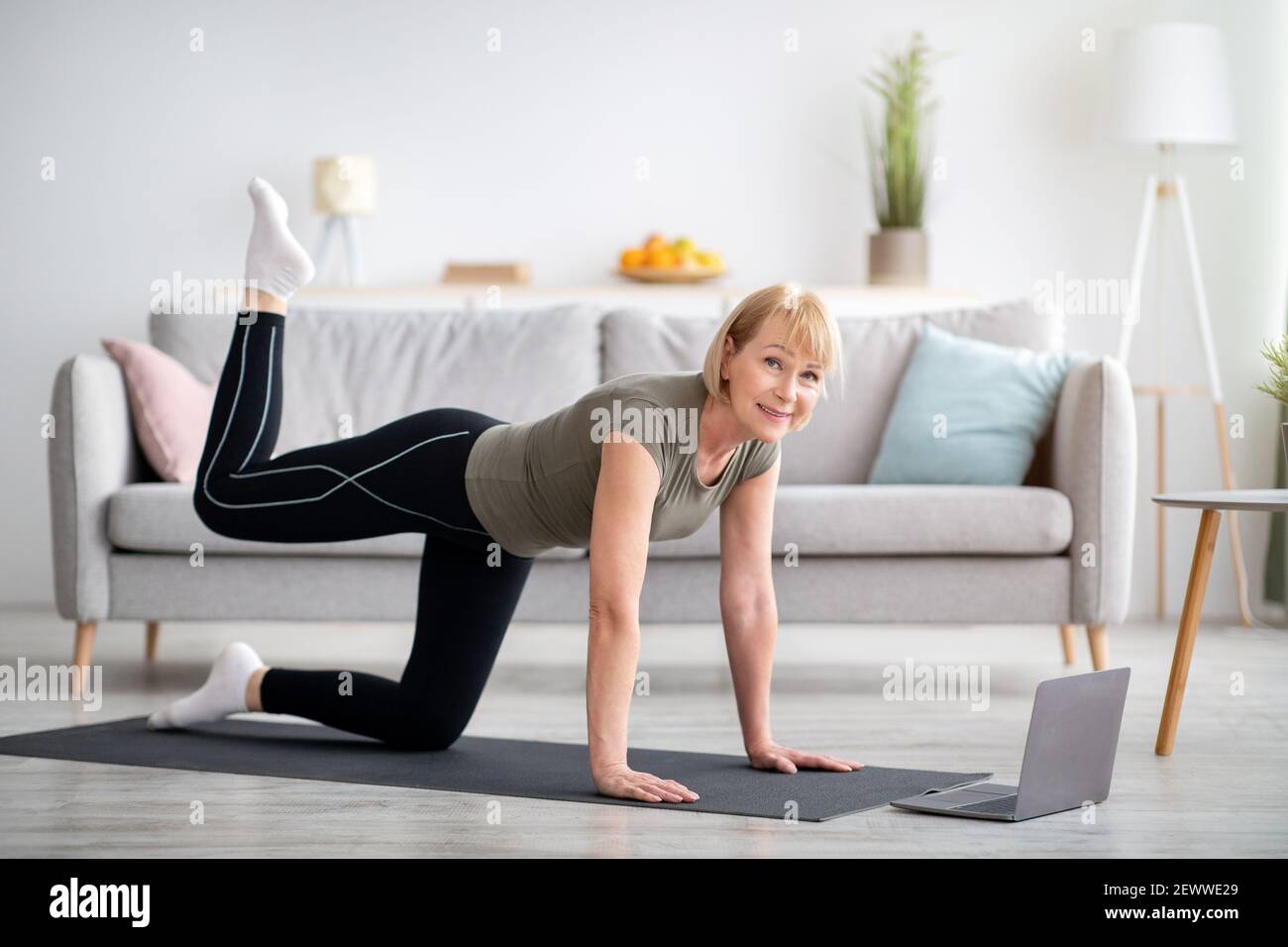 Online-Heimsport-Konzept. Sportliche ältere Frau, die im Wohnzimmer vor dem Laptop-Computer trainiert, Kopierplatz Stockfoto
