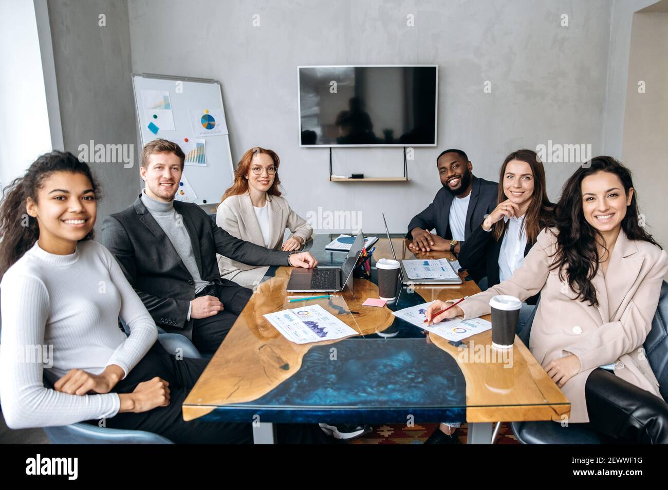 Porträt des erfolgreichen multirassischen Business-Team sitzt in modernen Büro. Gruppe von Geschäftsleuten arbeiten zusammen, lächeln, schauen auf die Kamera, Teamwork-Konzept Stockfoto