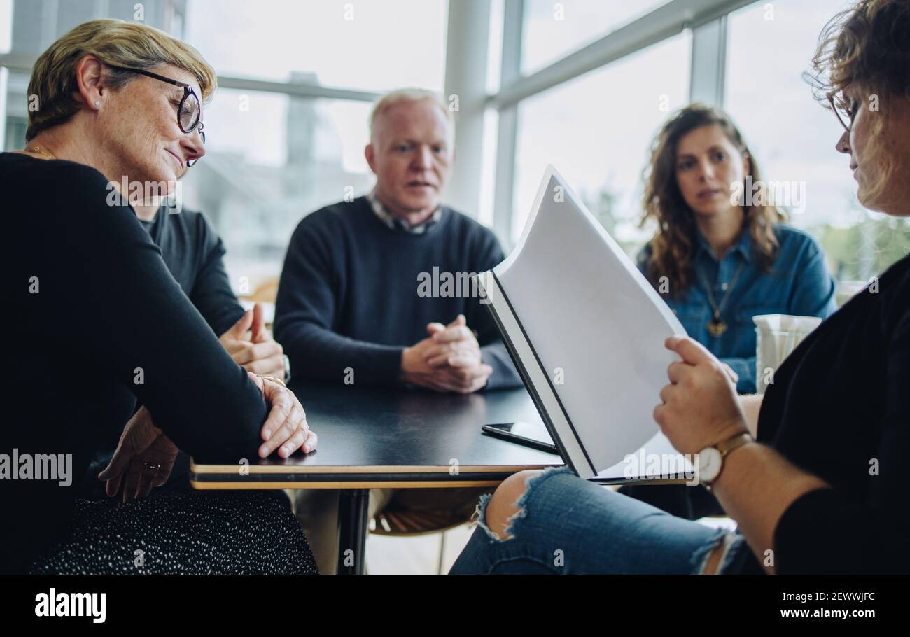 Geschäftsleute sitzen um einen Tisch und treffen sich mit einer Geschäftsfrau, die das Dokument liest. Besprechung des Geschäftsteams über einen neuen Vertrag. Stockfoto