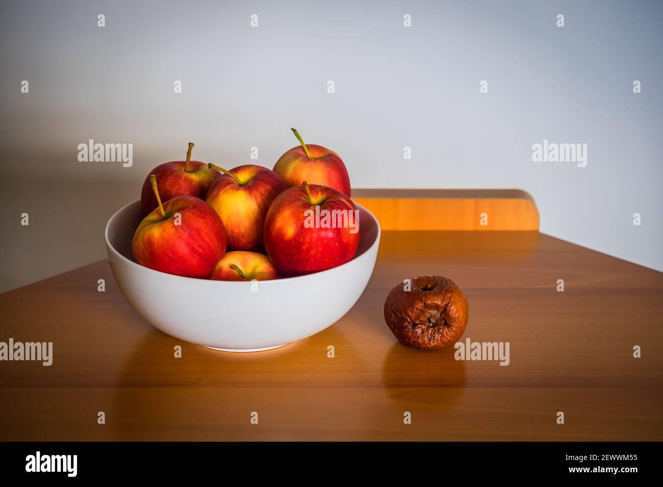 Ein fauler Apfel, der aus einer weißen Schale voller gefallen ist Gute Äpfel standen auf einem modernen Holztisch Stockfoto