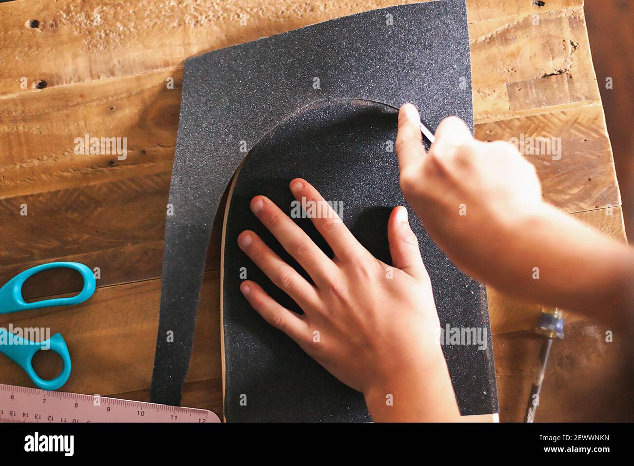 Boy Griff taping sein Skateboard auf einem Holztisch. Stockfoto