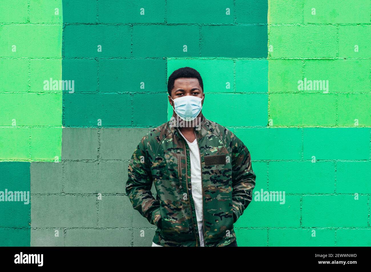 Afro amerikanischer schwarzer Junge auf grünem Wandhintergrund. Gekleidet in Militärjacke und Gesichtsmaske. Stockfoto