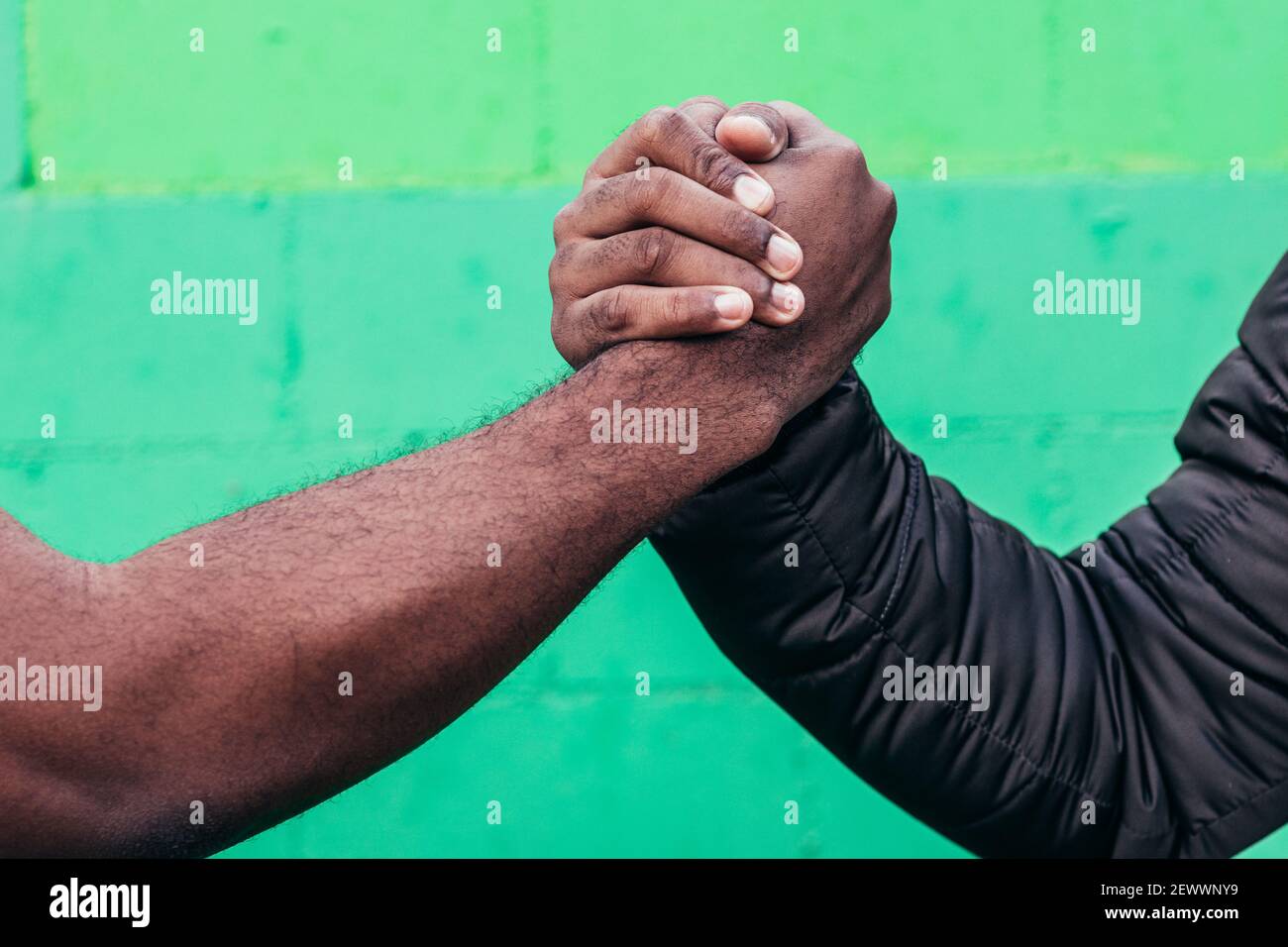 Zwei schwarze Jungen, die sich die Hände schüttelten. Nahaufnahme der Hände auf grünem Wandhintergrund. Stockfoto