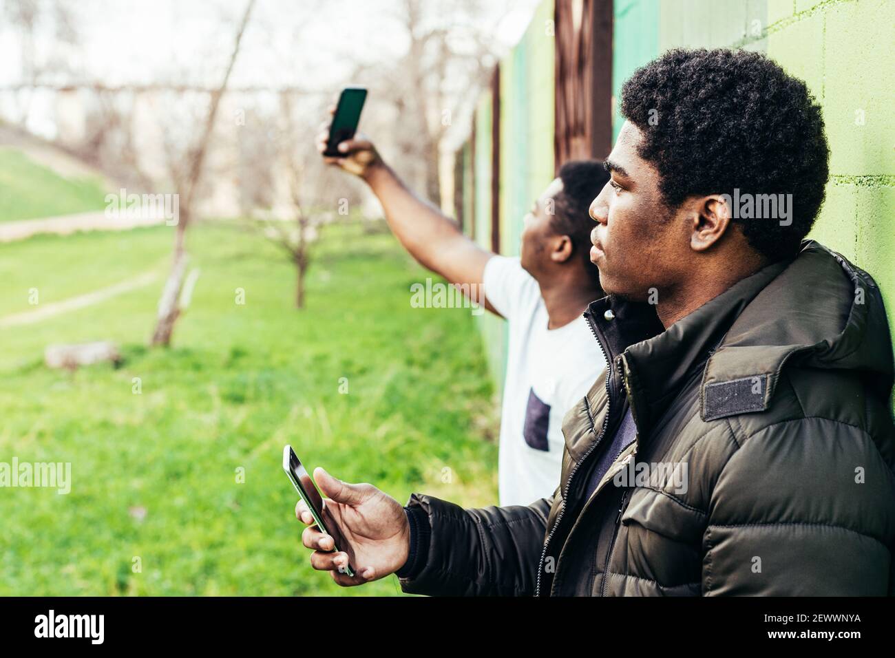 Portrait von zwei schwarzen Jungen, die sich an einer grünen Wand lehnen. Mit ihren Mobiltelefonen. Stockfoto