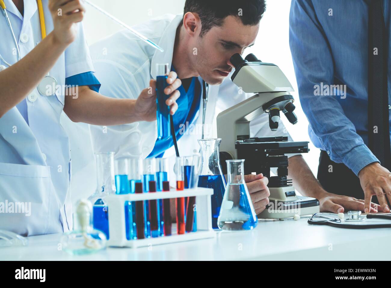 Gruppe von Wissenschaftlern mit Labormantel, die im Labor arbeiten, während sie biochemische Proben in Reagenzglas und wissenschaftlichen Instrumenten untersuchen. Wissenschaft Stockfoto