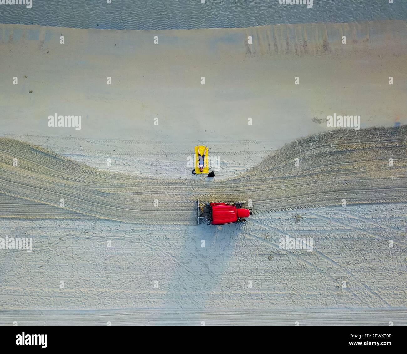 Genießen Sie den tropischen Strand auf gelben Handtuch, sehr früh am Morgen. Roter Traktor putzt den Strand. Luftaufnahme von oben nach unten Stockfoto