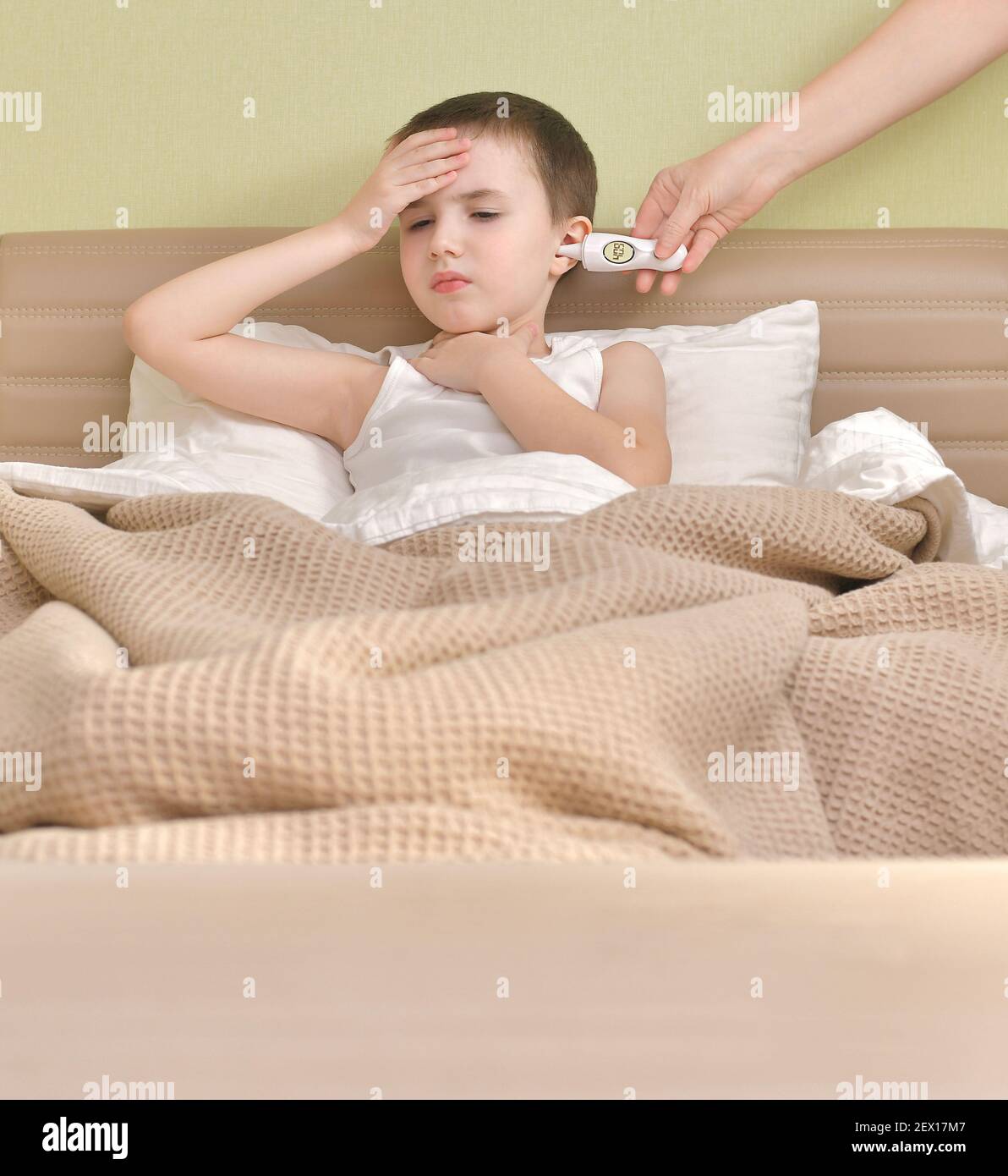 Ein krankes Kind liegt im Bett. Messung der erhöhten Temperatur mit einem Ohrthermometer. Stockfoto