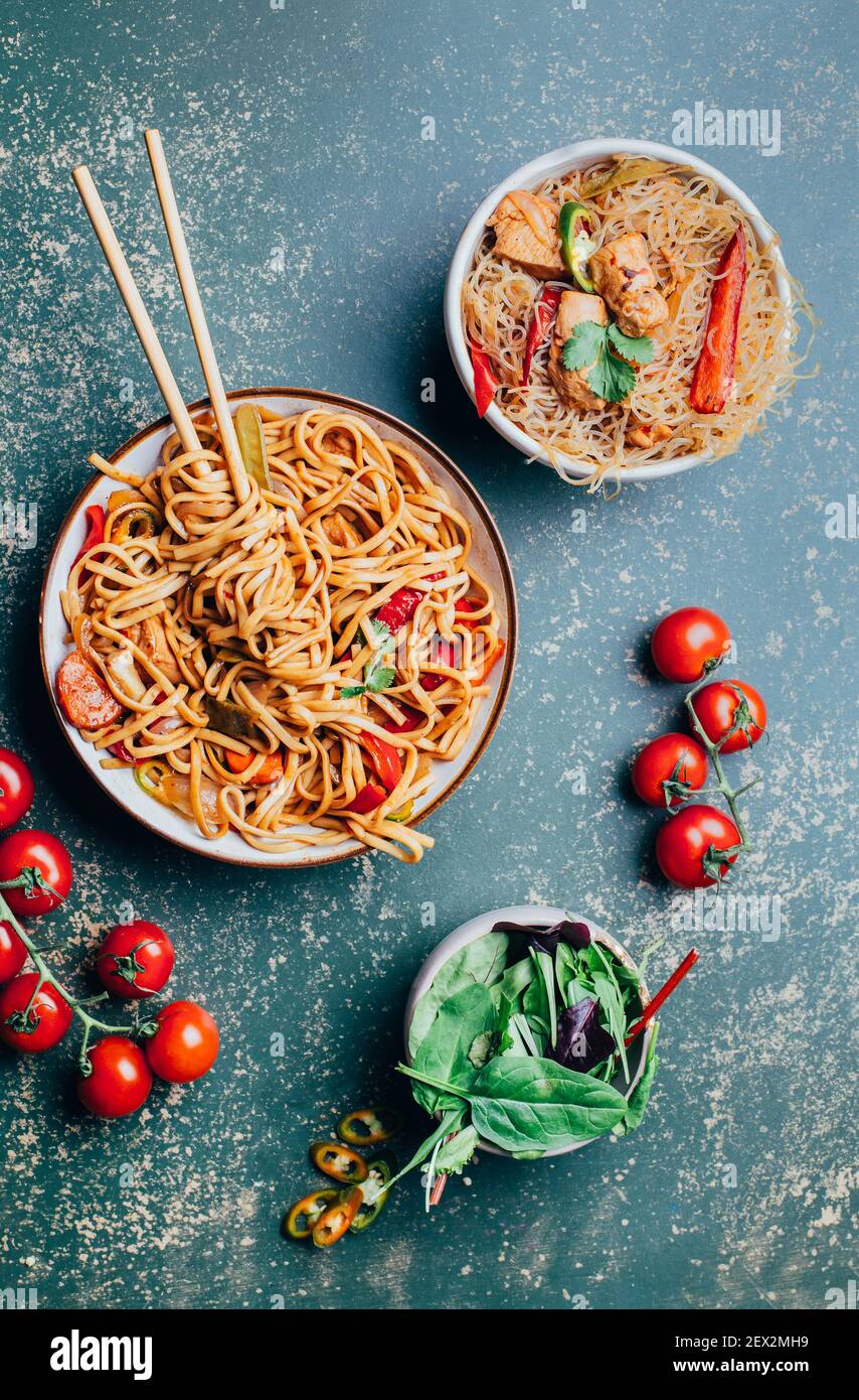Nahaufnahme eines Tellers chinesischer Nudeln mit Fleisch und Gemüse in Tellern und chinesische Essstäbchen auf grünem Hintergrund Stockfoto