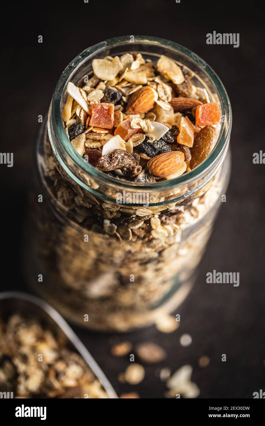 Frühstücksflocken im Glas. Gesundes Müsli mit Haferflocken, Nüssen und Rosinen auf schwarzem Tisch. Stockfoto