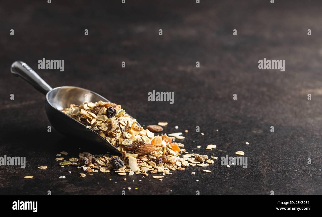 Frühstücksflocken in einem Messlöffel. Gesundes Müsli mit Haferflocken, Nüssen und Rosinen auf schwarzem Tisch. Stockfoto