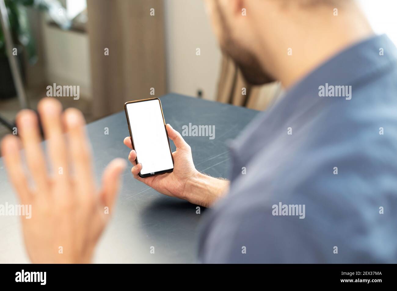 Konzentrieren Sie sich auf den Telefonbildschirm, Rückansicht des männlichen Mitarbeiters, der spricht, während eines Videoanrufs spricht, winkende Hand, Webcam-Gruppenkonferenz, im Büro, Kopierbereich, Mock-up, leerer Raum Stockfoto