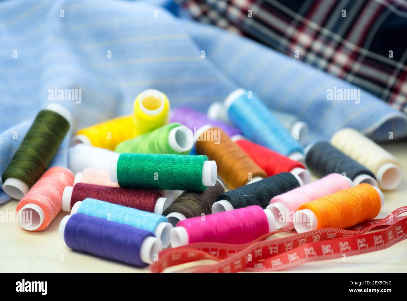 Set von bunten Nähfäden, Nahaufnahme. Stoff zum Nähen im Hintergrund. Stockfoto