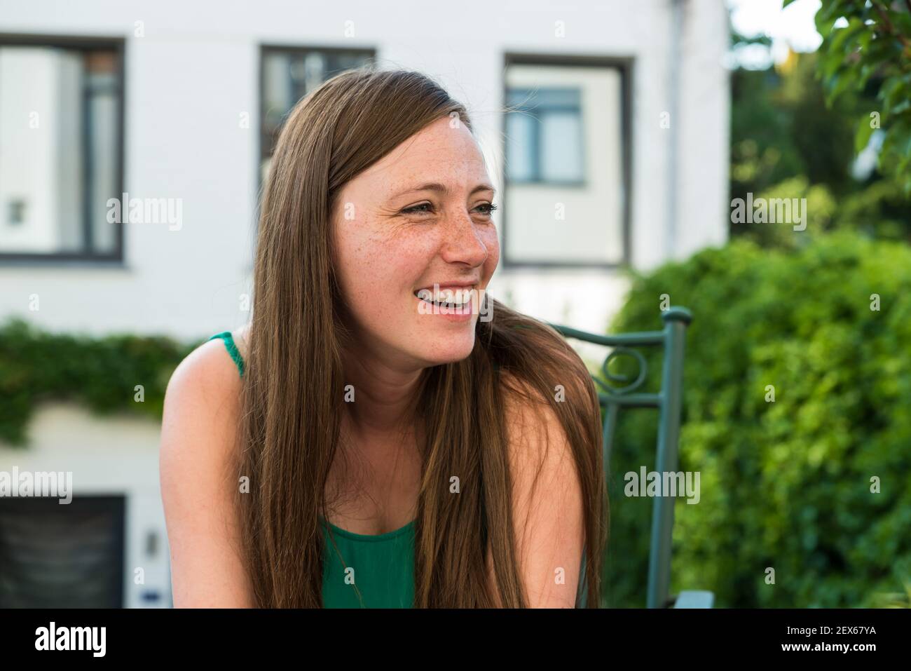 Porträt einer attraktiven dreißig Jahre alten Frau, lächelnd in der Sonne auf ihrer Terrasse im Sommer Stockfoto