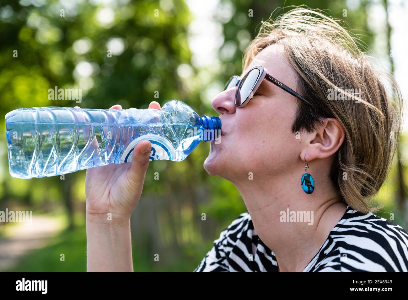 Uccle, Brüssel Hauptstadt Region / Belgien - 05 17 2020: Attraktives 30-jähriges Mädchen trinkt eine Flasche Mineralwasser Stockfoto