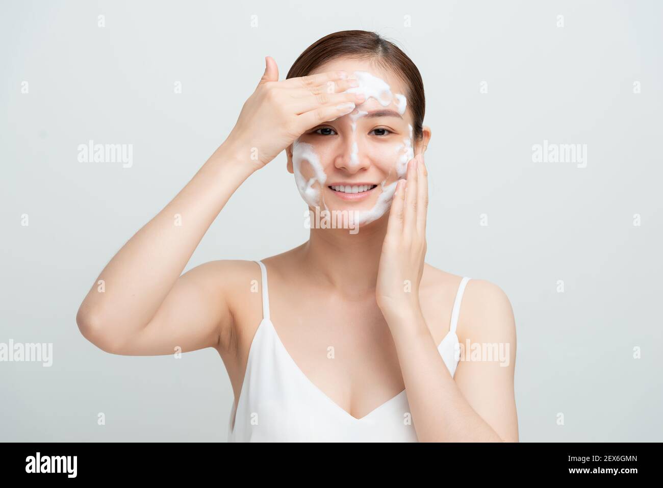 Lächelnd schöne asiatische Mädchen mit schäumenden Reinigungsmittel. Gesichtswaschkonzept isoliert auf weißem Hintergrund. Stockfoto