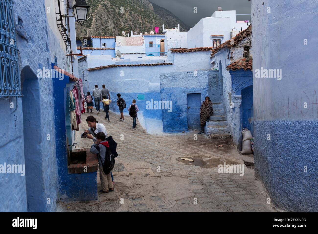 Marokko, Chefchaouen, Architektur von weißen und indigo gekalkten Gebäuden mit Kindern am kommunalen Wasserbrunnen Stockfoto