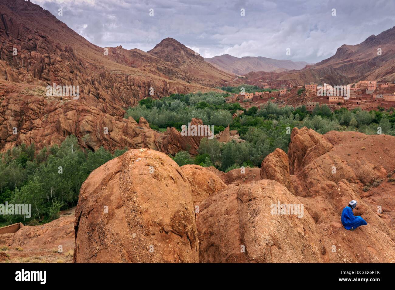 Marokko, Dades Valley in der Nähe der 'Monkey Paws' Felsformationen, mit Berber Männchen in blau gekleidet. Eine karge Landschaft mit üppiger Vegetation entlang eines Flusses. Stockfoto