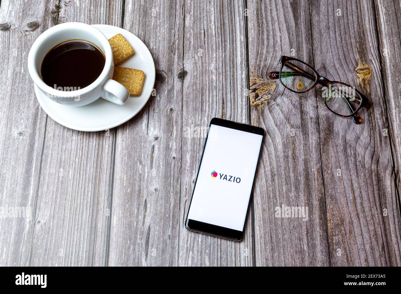 Ein Handy oder Handy auf einem Holz gelegt Tabelle mit der YAZIO Kalorienzähler App geöffnet neben Ein Kaffee Stockfoto