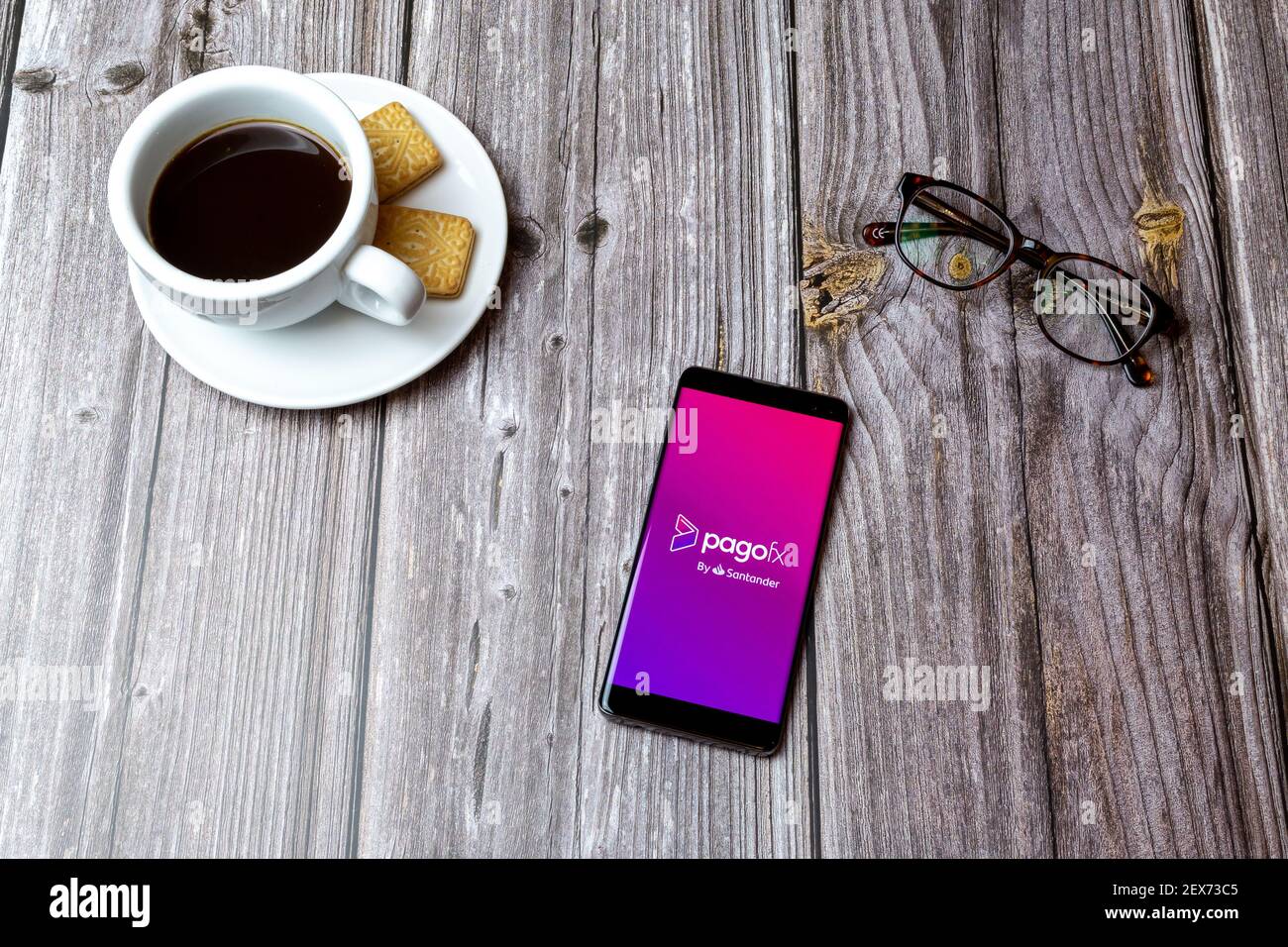 Ein Handy oder Handy auf einem Holz gelegt Tabelle mit der PagoFX Geldtransfer-App geöffnet neben Ein Kaffee Stockfoto