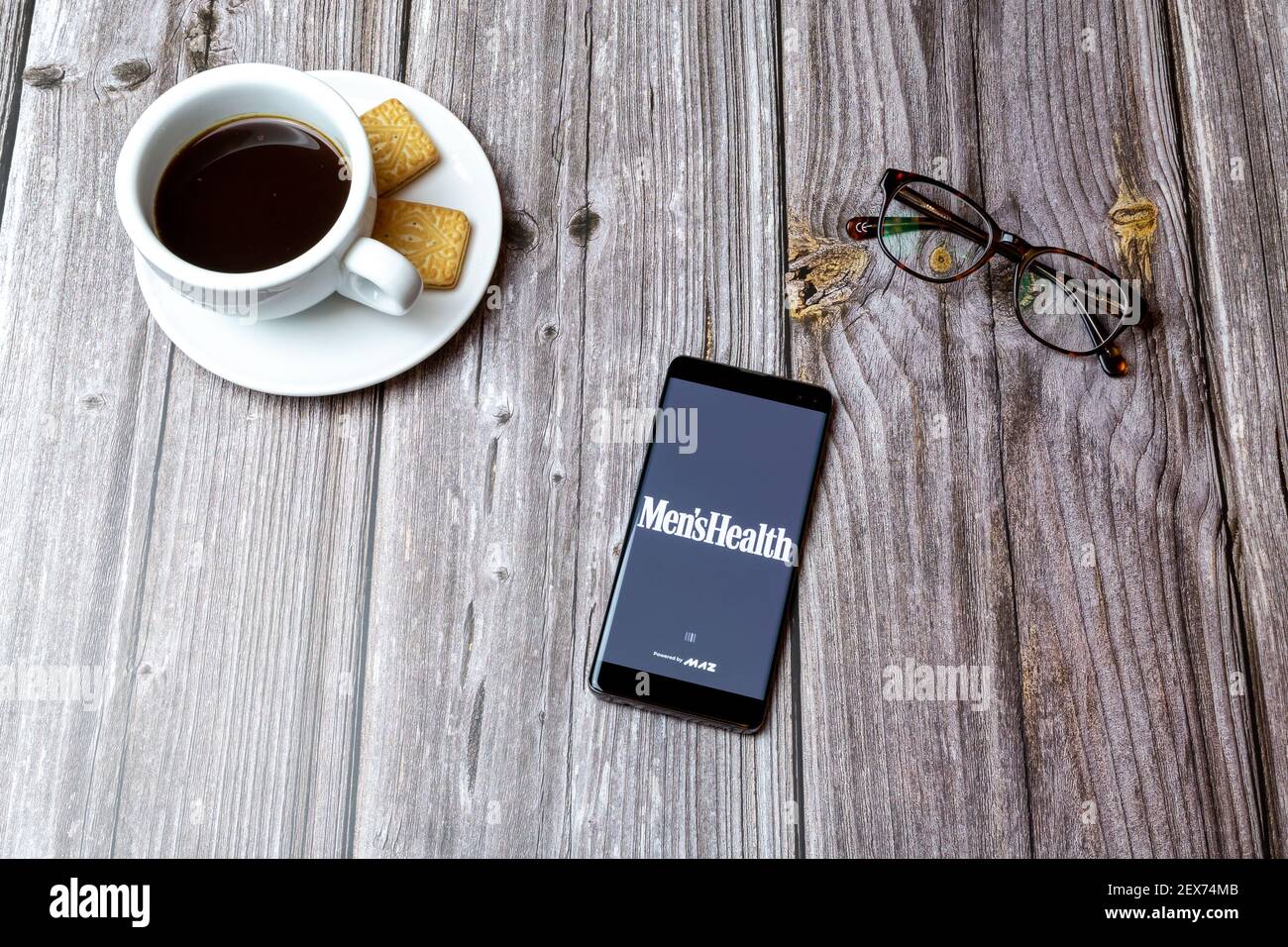 Ein Handy oder Handy auf einem Holz gelegt Tabelle mit der Herren Gesundheit App geöffnet neben einem Kaffee Stockfoto
