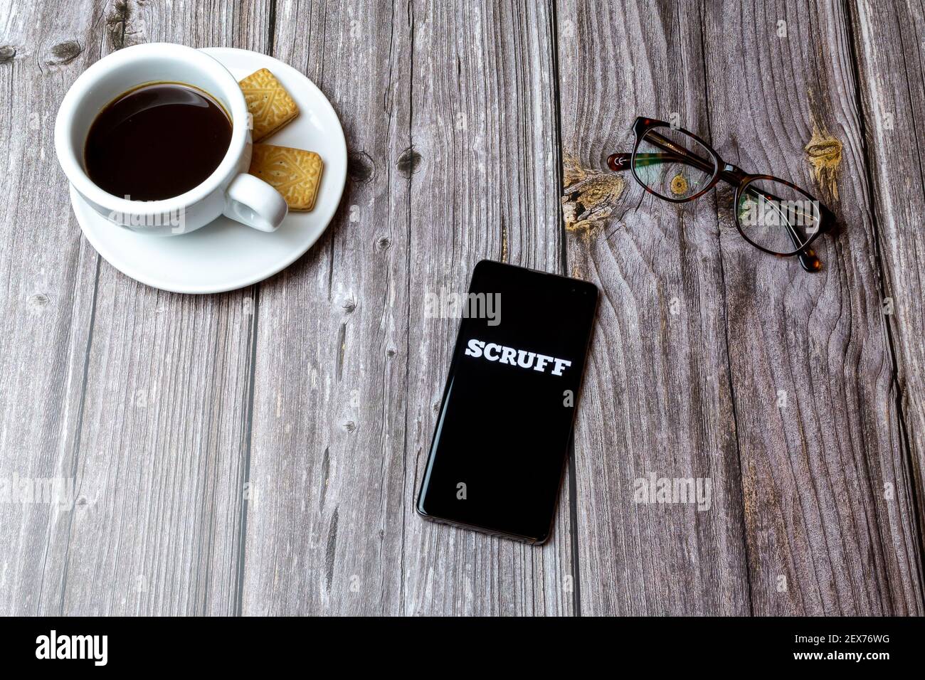 Ein Handy oder Handy auf einem Holz gelegt Tabelle mit dem scruff Gay Chat App geöffnet neben Ein Kaffee Stockfoto