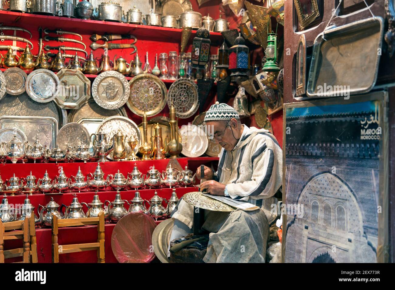 Ein silberner schmied, der in einem Geschäft an seinen Waren arbeitet, zeigt Silberteller, Teekannen und Tabletts Stockfoto