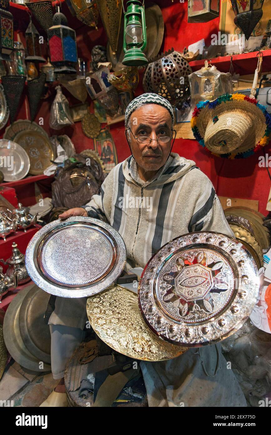 Ein silberner schmied, der in einem Geschäft an seinen Waren arbeitet, zeigt Silberteller, Teekannen und Tabletts Stockfoto