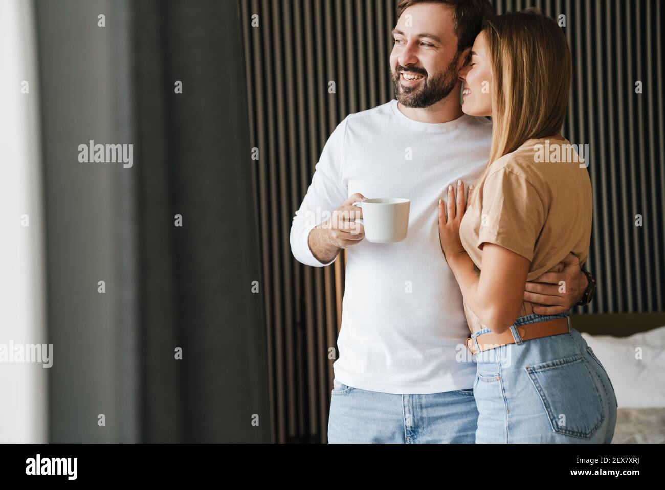 Glückliches junges Paar umarmt beim Stehen und mit Kaffee in Das Schlafzimmer Stockfoto