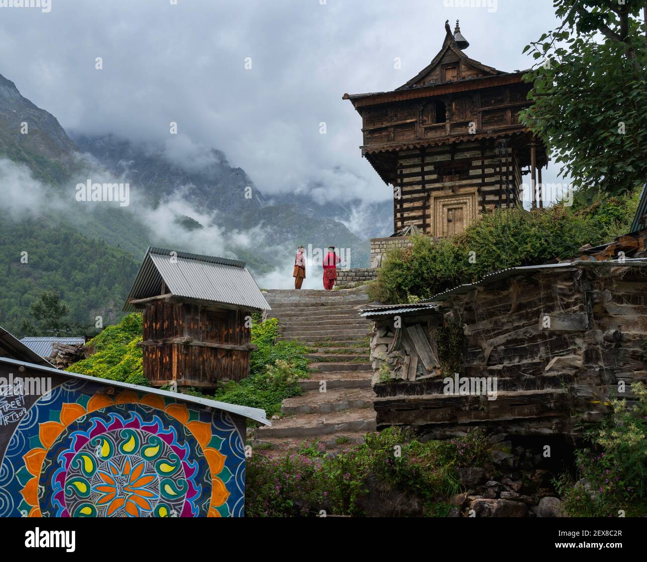 Zwei Frauen in Diskussion neben kleinen Tempel und flankiert von Himalaya unter niedriger Wolke in Chitkul, Himachal Pradesh, Indien. Stockfoto