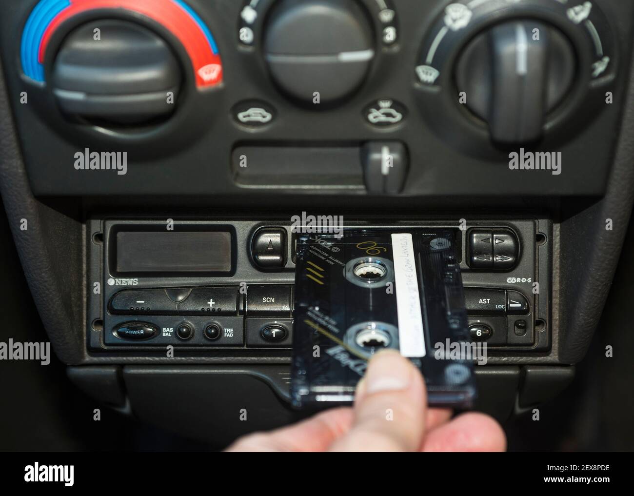 Eine Hand, die ein Musikkassettenband in das Kassettendeck eines Autos legt. Stockfoto
