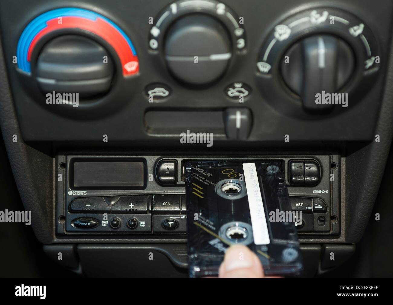 Eine Hand, die ein Musikkassettenband in das Kassettendeck eines Autos legt. Stockfoto
