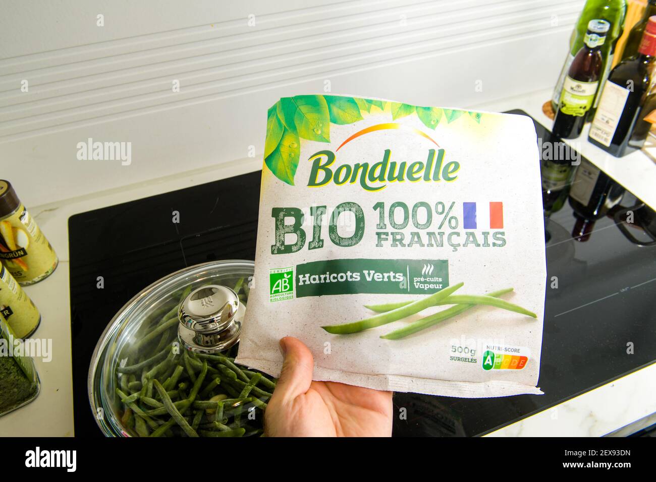 Paris, Frankreich - Mar 2, 2021: POV männliche Hand hält über Induktionsplatte das Paket von Bonduelle Bio 100 Prozent französisch String Bohnen grün Paket Stockfoto