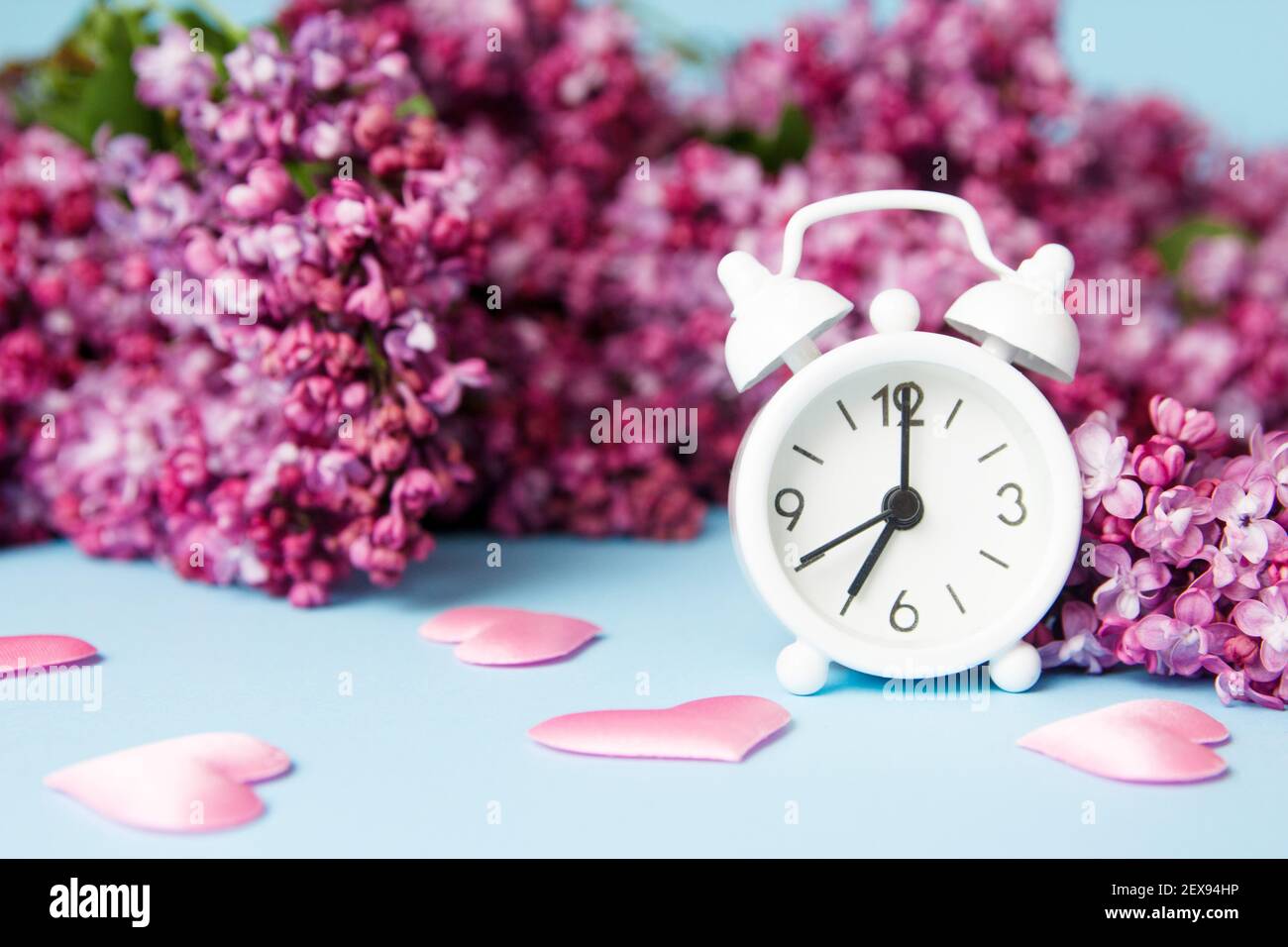 Flieder Blumen mit vintage winzig Wecker auf blauem Hintergrund. Frühlingshafte Morgenkonzeption. Stockfoto