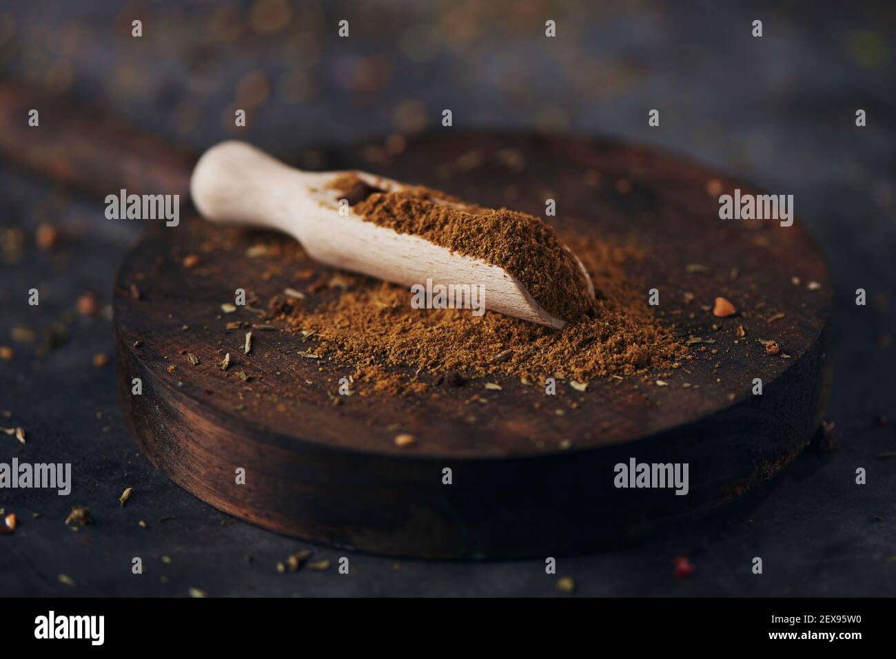 Eine hölzerne Messlöffel voll Garam Masala, ein beliebtes Gewürz in der südasiatischen Küche, auf einem Holztablett, auf dunkler Steinoberfläche platziert Stockfoto