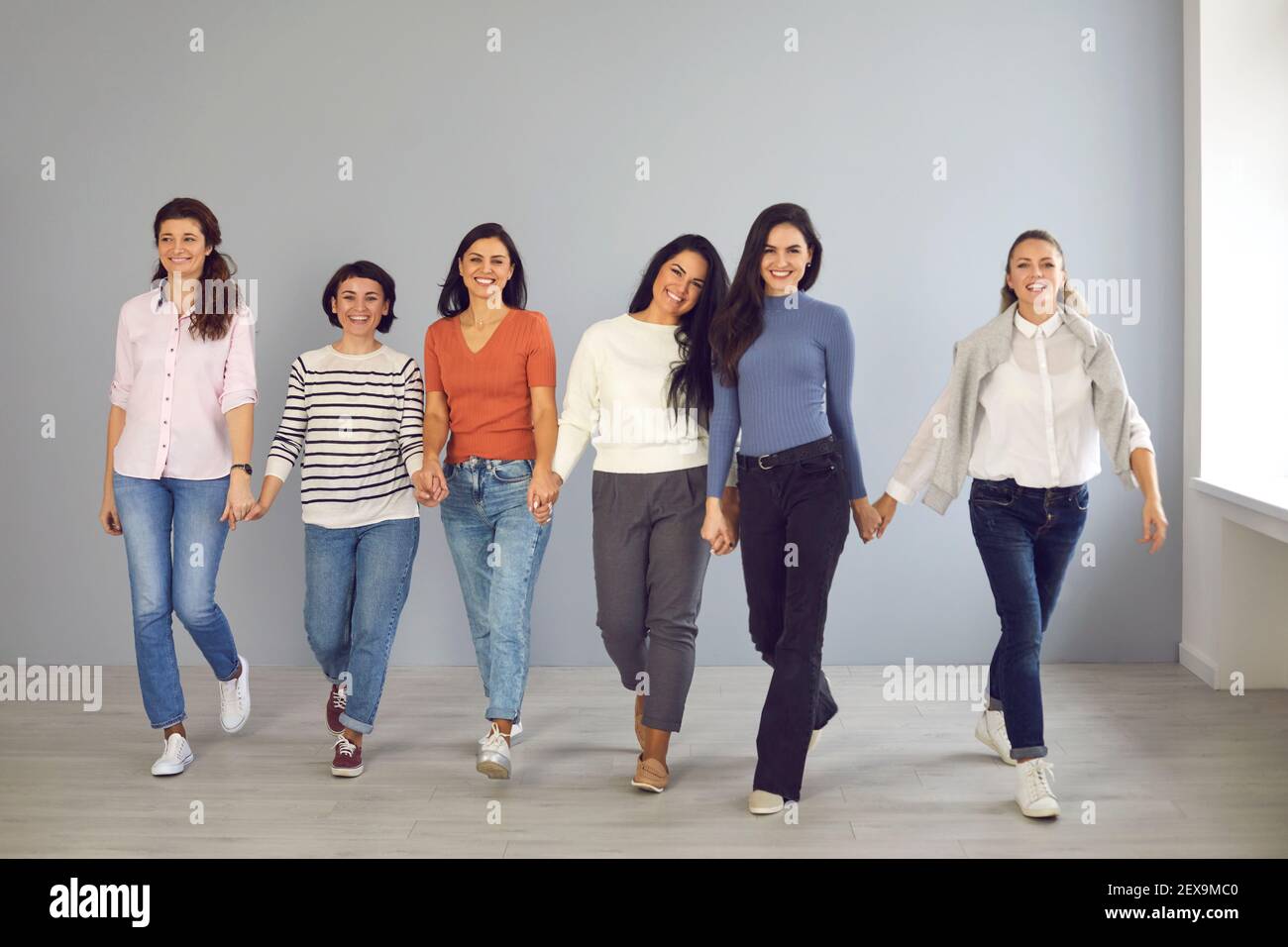 Gruppe von glücklichen selbstbewussten unterstützenden jungen Frauen gehen Hand in Hand und Lächeln Stockfoto