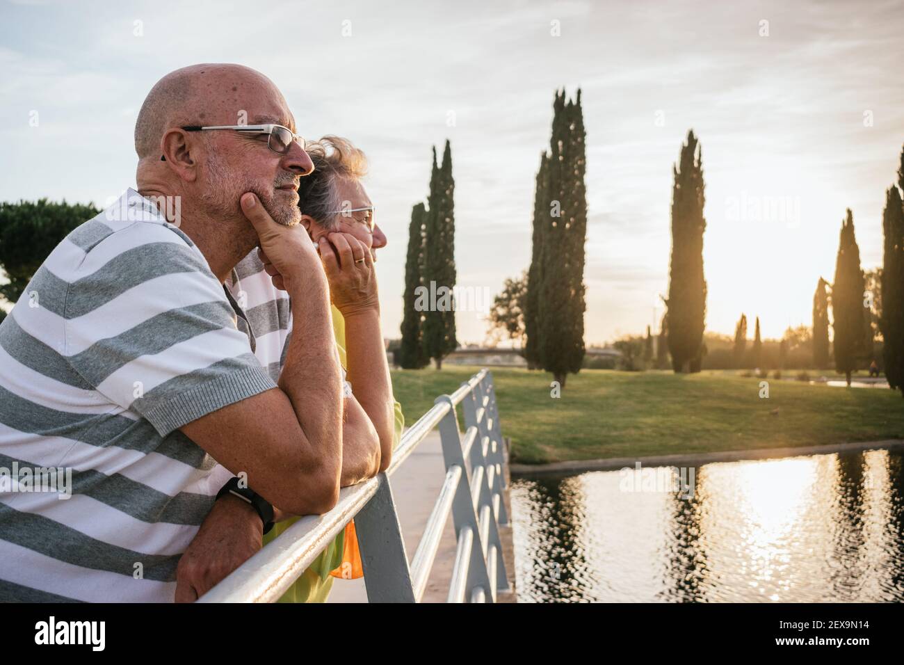Rentnerpaar, das den Sonnenuntergang von einer Brücke aus beobachtet Stockfoto
