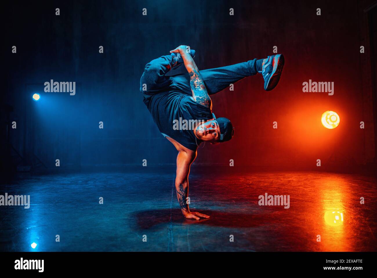 Junger Mann bricht Tanz in dunklen Halle mit blauen und roten Lichtern. Tätowierung auf Händen. Stockfoto