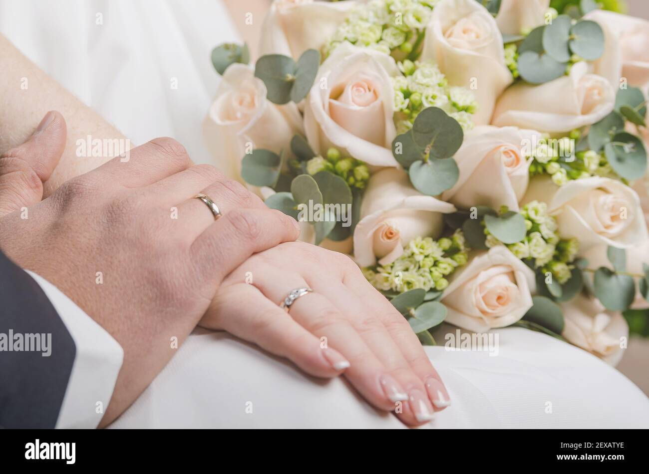 Die Hände der Braut und des Bräutigams. Die Handfläche eines Mannes liegt auf der einer Frau. Oben ist ein Bouquet von Teerosen. Hochzeit. Stockfoto