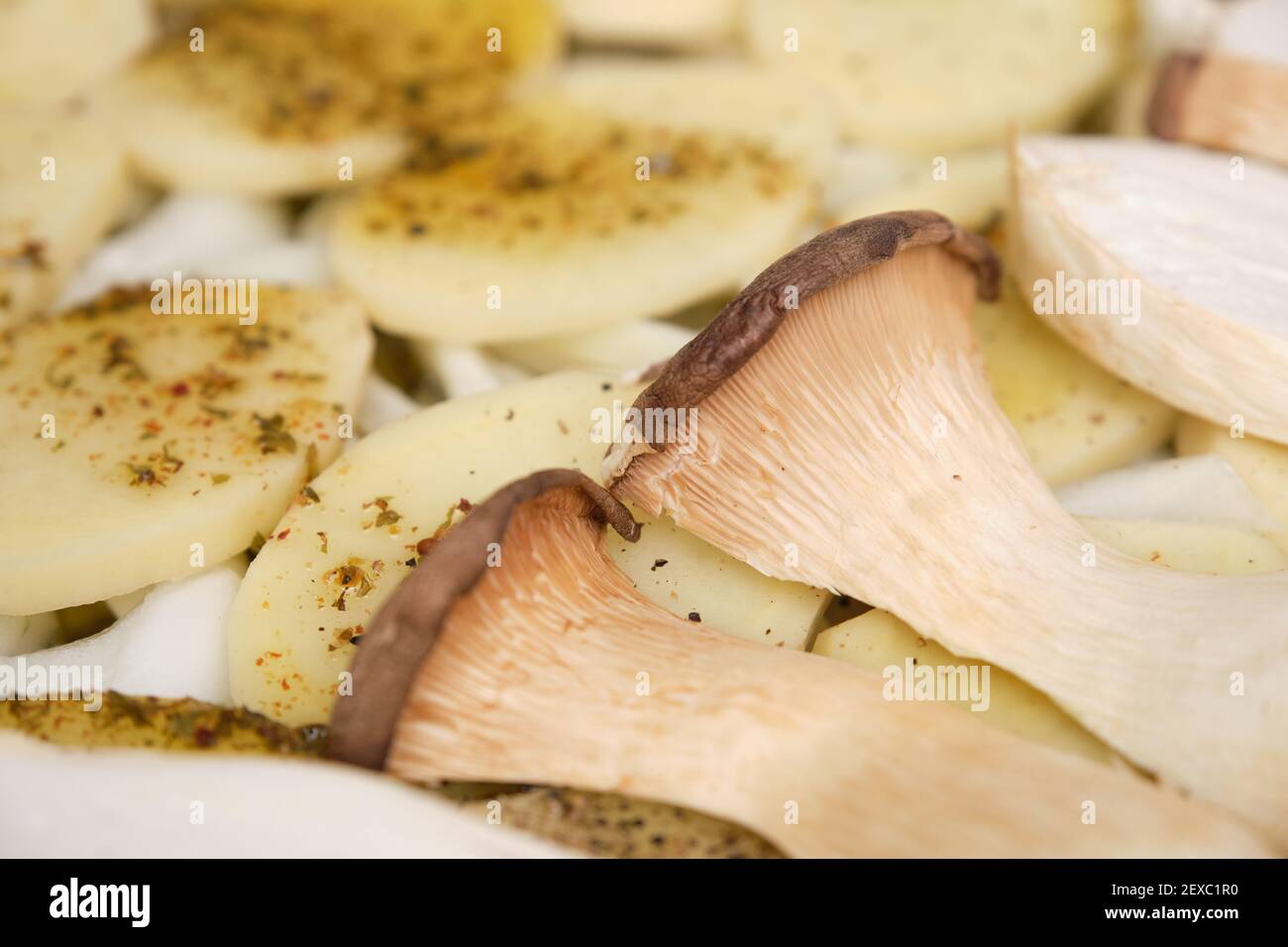 Nahaufnahme von in Scheiben geschnittenen Trompetenpilzen (pleurotus eryngii) über gewürzten Kartoffeln und Zwiebeln. Kochvorgang. Mediterrane Ernährung. Stockfoto