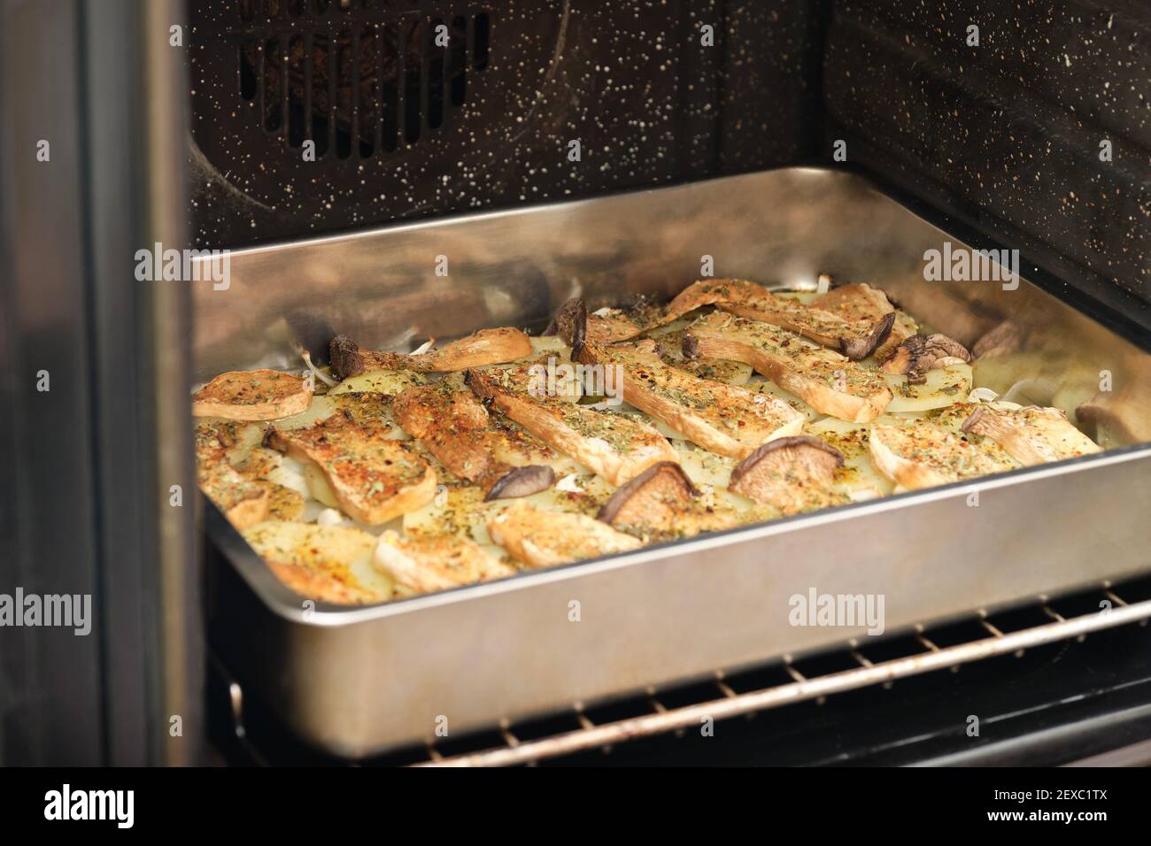 Tablett mit gewürzten geschnittenen Trompetenpilzen (pleurotus eryngii), Kartoffeln und Zwiebeln im Ofen. Mediterrane Ernährung. Stockfoto
