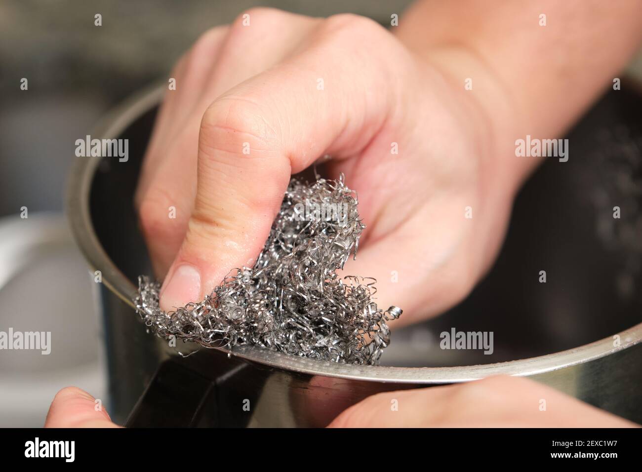 Zugeschnittenes Bild eines Mannes Hände waschen einen Topf oder das Geschirr mit einem Edelstahl Schwamm Schrubber tun. Reinigung der Hausarbeiten. Stockfoto