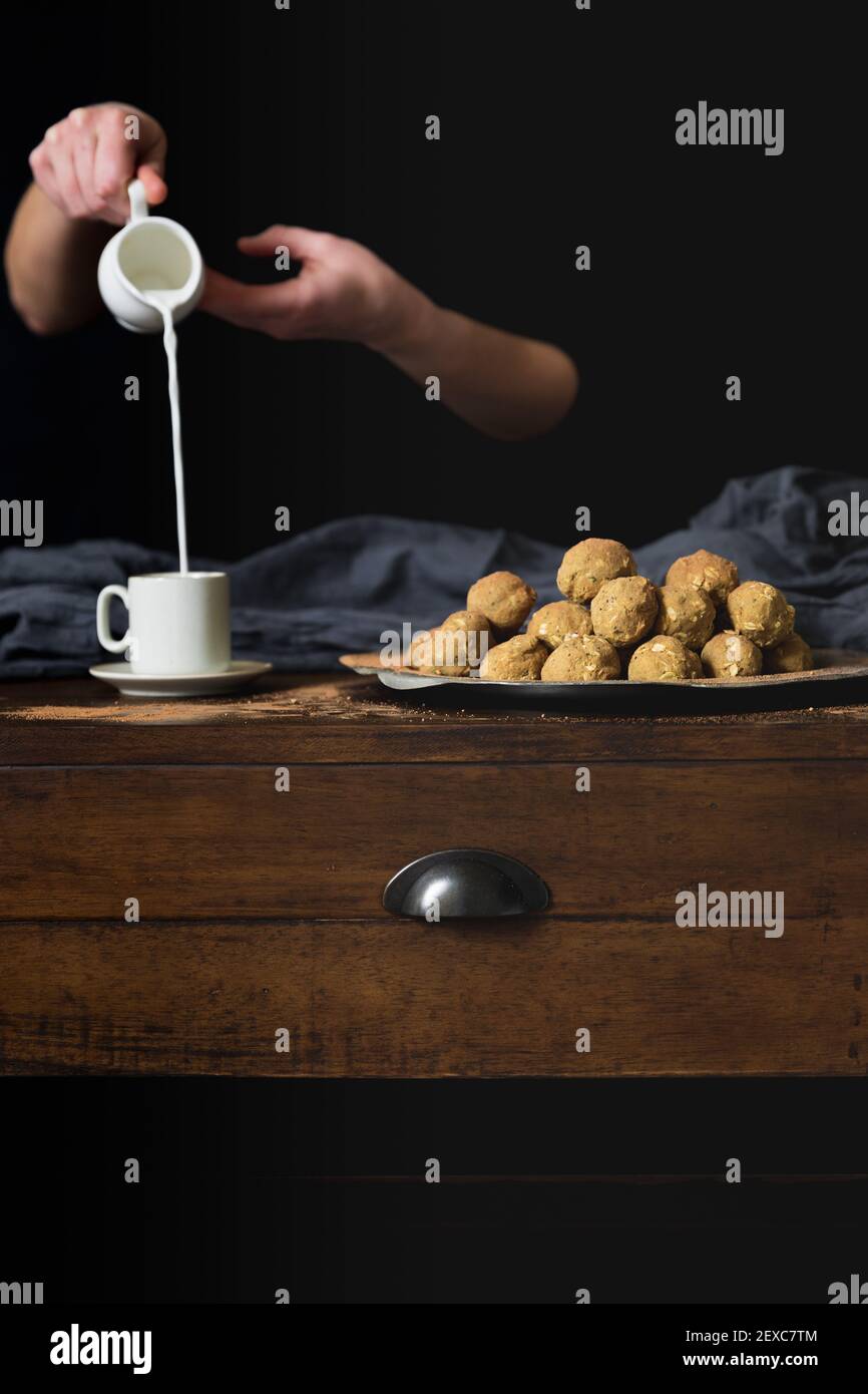 Eine Hand, die einen Krug hält, gießt Milch in einen Becher Neben Proteinbällen Stockfoto