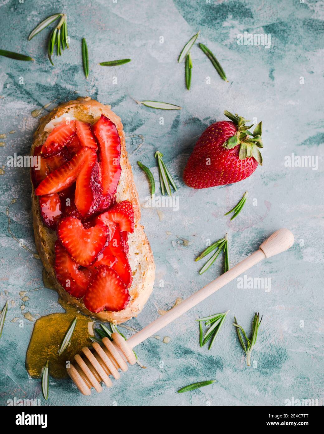 Erdbeeren auf Toast mit verstreutetem Rosmarin und einem tropfenden Honig Zauberstab Stockfoto